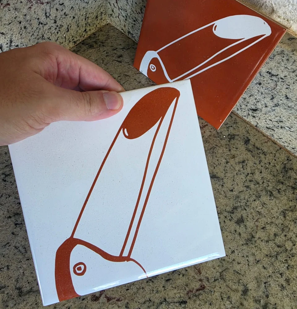 Dois azulejos cerâmicos com a ilustração de um tucano impressa, um branco e um terracota